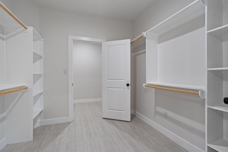 Spacious walk-in closet featuring light wood-finish flooring, ample white shelving, and multiple clothing rods