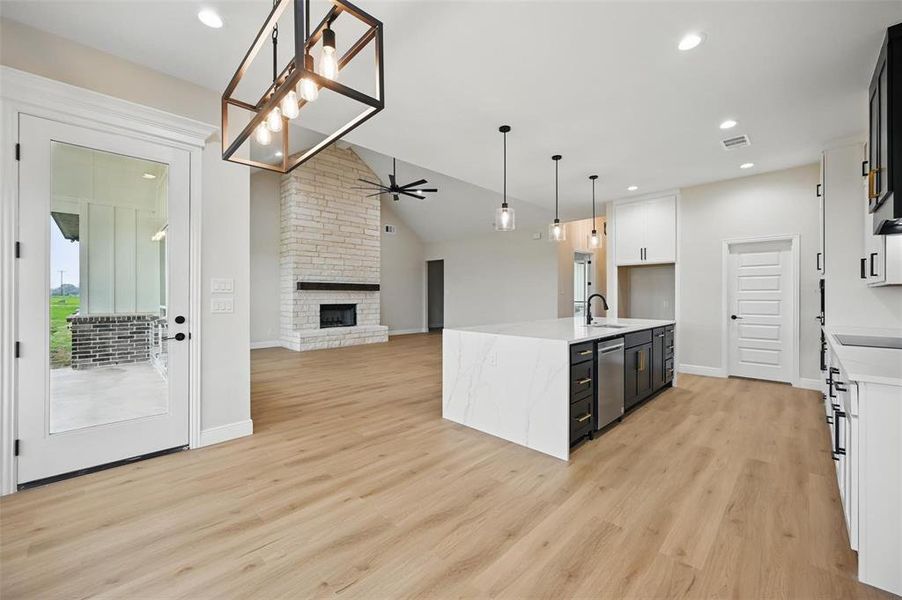 Kitchen featuring dark cabinets, vaulted ceiling, open floor plan, light stone countertops, and a stone fireplace Kitchen featuring dark cabinets, vaulted ceiling, open floor plan, light stone countertops, and a stone fireplace