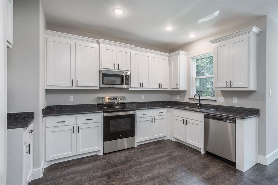 Kitchen featuring stainless steel appliances, white cabinets, dark stone counters, dark wood-type flooring, and recessed lighting Kitchen featuring stainless steel appliances, white cabinets, dark stone counters, dark wood-type flooring, and recessed lighting