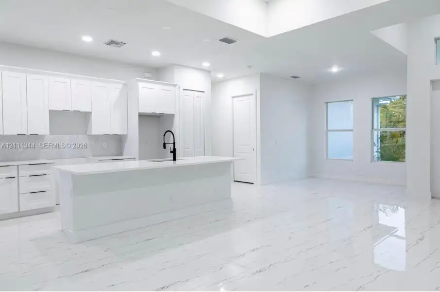 Kitchen featuring white shaker-style cabinetry, a central island with a quartz countertop, matte black faucet hardware, high-gloss patterned flooring, and recessed ceiling lighting Kitchen featuring white shaker-style cabinetry, a central island with a quartz countertop, matte black faucet hardware, high-gloss patterned flooring, and recessed ceiling lighting