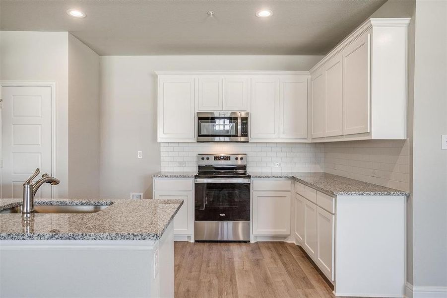 Kitchen featuring stainless steel appliances, light stone counters, white cabinetry, light wood finished floors, and recessed lighting