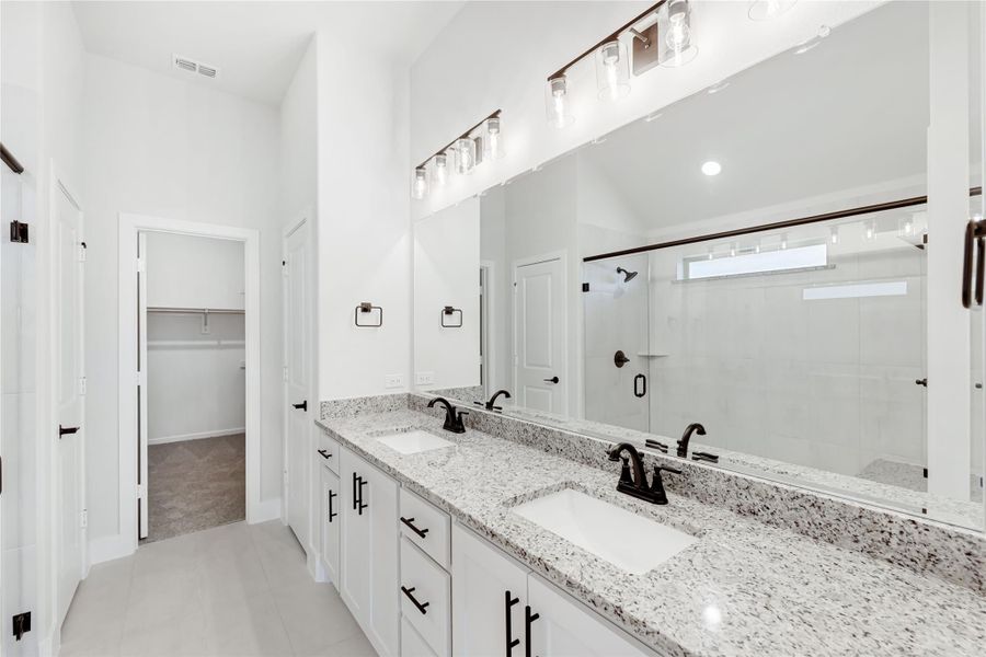 Master bathroom with double vanity, granite countertops, white cabinets, and walk-in closet visible in background