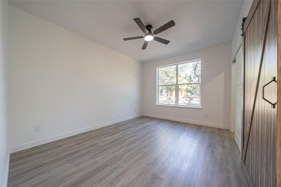 Unfurnished bedroom featuring a barn door, wood finished floors, a closet, and a ceiling fan