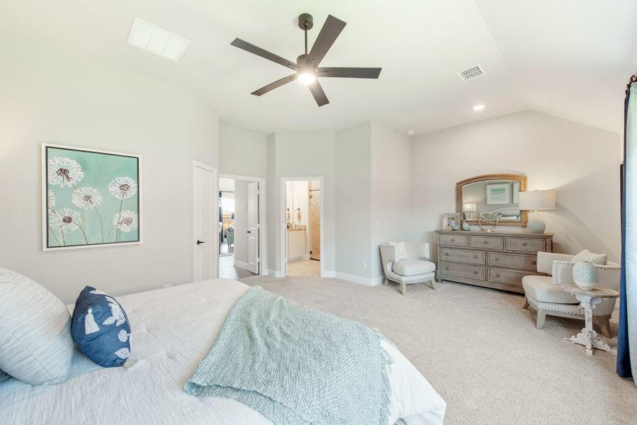 Spacious master bedroom with vaulted ceiling, ceiling fan, dresser with mirror, and ensuite bathroom doorway
