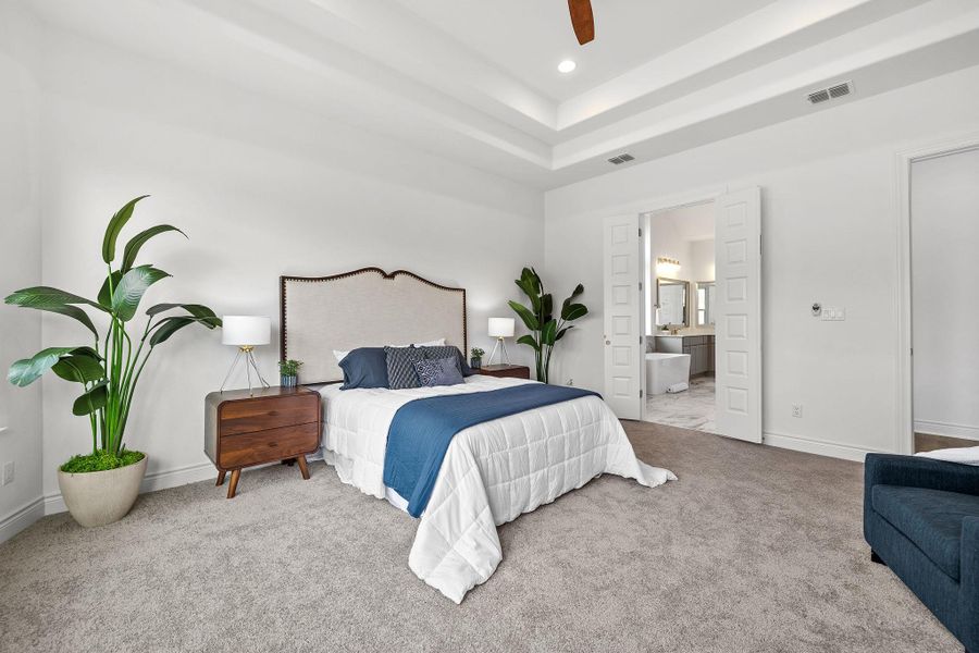 Carpeted bedroom featuring recessed lighting, a tray ceiling, ensuite bathroom, and a ceiling fan