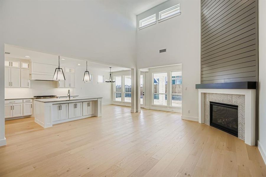 Unfurnished living room featuring light wood-style flooring, a fireplace, a chandelier, and a high ceiling Unfurnished living room featuring light wood-style flooring, a fireplace, a chandelier, and a high ceiling