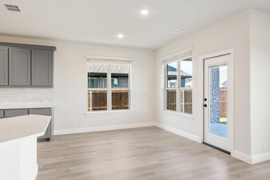 Open dining area with light wood floors, white walls, and glass back door next to large windows Open dining area with light wood floors, white walls, and glass back door next to large windows