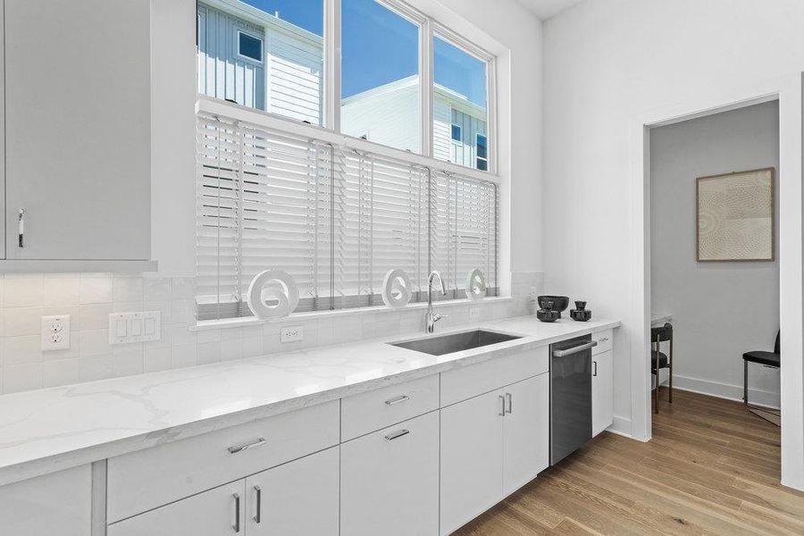 Kitchen featuring light stone countertops, white cabinets, light wood finished floors, and stainless steel dishwasher