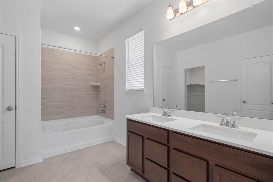 This primary bathroom is definitely move-in ready! Featuring an oversized tub and shower combo with tile surround, stained cabinets with light countertops, dual vanities, high ceilings, neutral paint, sleek and modern finishes.