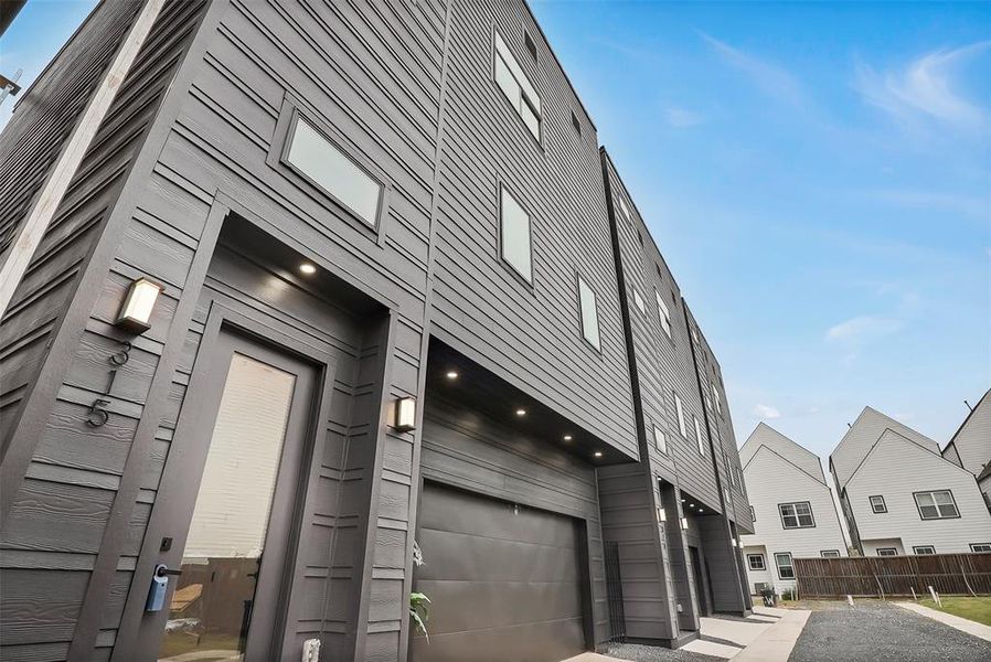 Modern three-story townhome with sleek black exterior, large windows, and a garage. It features contemporary design elements and is situated in a neatly arranged residential area.