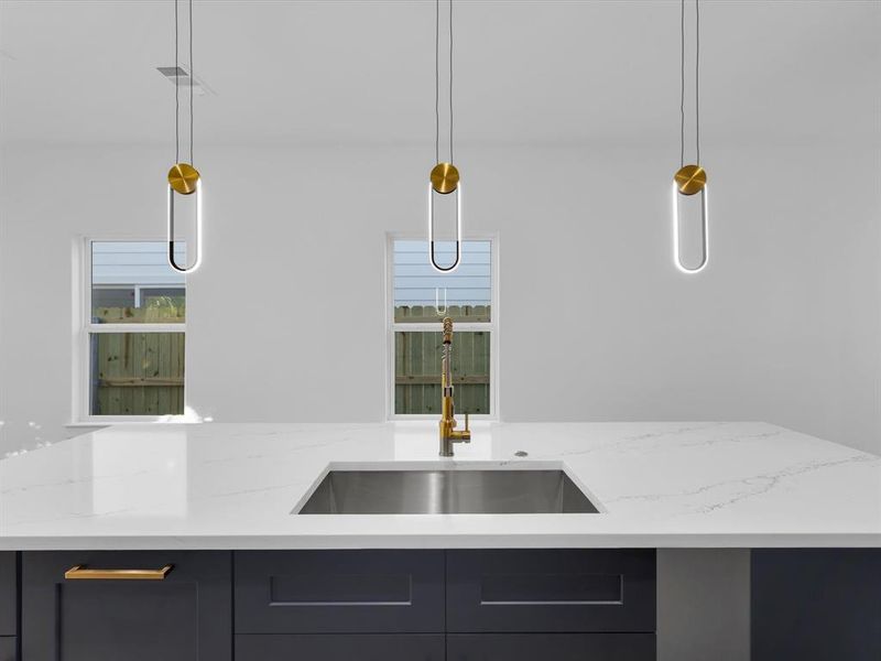 Kitchen featuring light stone countertops, pendant lighting, plenty of natural light, and sink