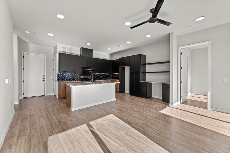 Kitchen with sink, light hardwood / wood-style flooring, an island with sink, ceiling fan, and decorative backsplash