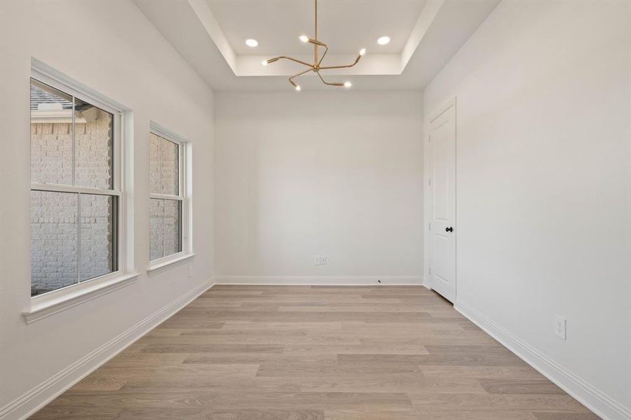 Spare room featuring light wood-type flooring, a tray ceiling, baseboards, and recessed lighting