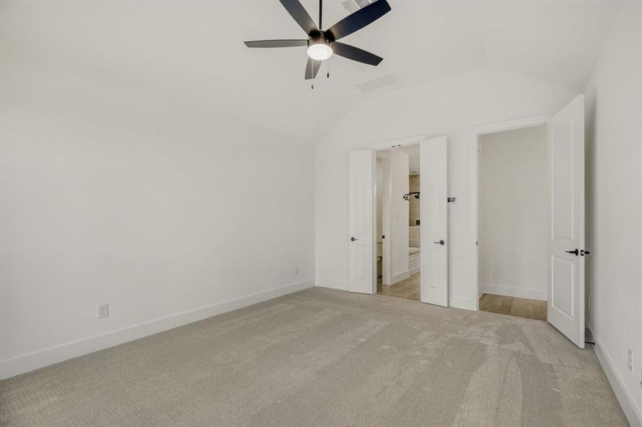 Unfurnished bedroom with light colored carpet, lofted ceiling, a ceiling fan, and ensuite bath