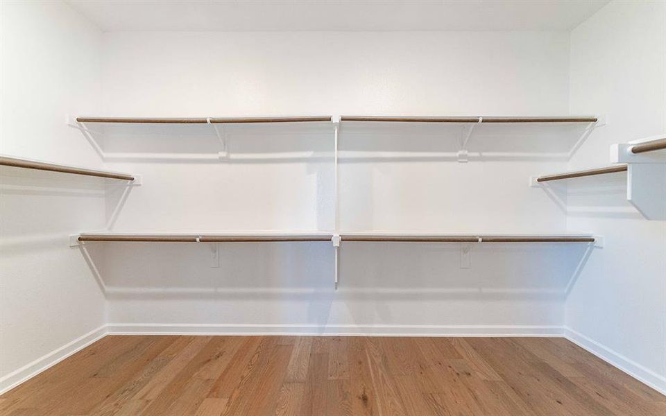 Bright interior space featuring wood-finish flooring, white walls, and extensive built-in shelving with hanging rods Bright interior space featuring wood-finish flooring, white walls, and extensive built-in shelving with hanging rods