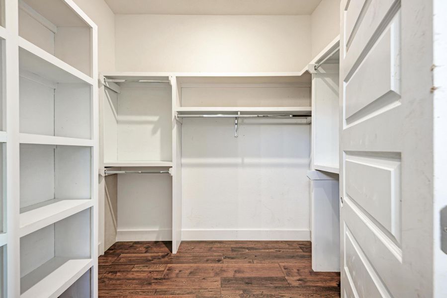Rich wood flooring anchors this generous storage space featuring integrated custom shelving and hanging rods.