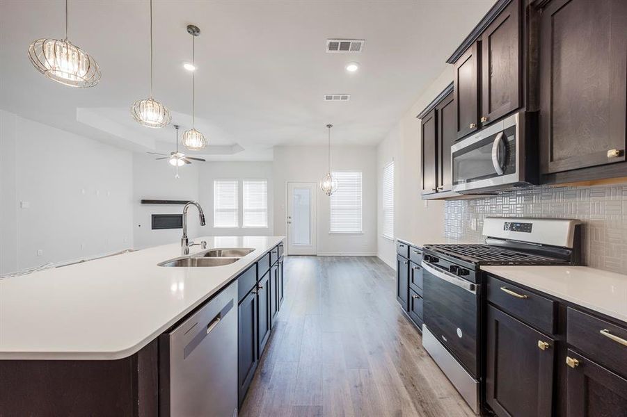 Kitchen with a center island with sink, sink, backsplash, pendant lighting, and stainless steel appliances