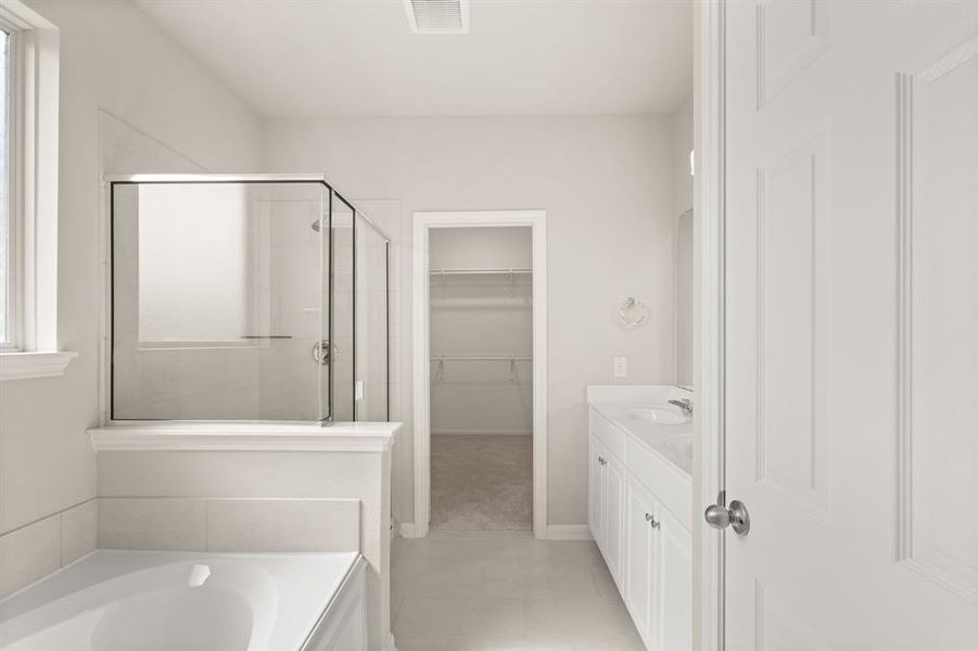 This additional view of your primary bathroom features tile flooring, fresh paint, walk-in shower, a separate garden tub, and a large walk-in closet.