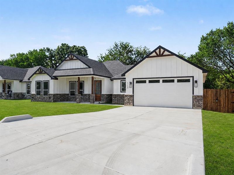 Modern farmhouse exterior featuring white board and batten siding, dark stone accents, and a contrasting dark roof Modern farmhouse exterior featuring white board and batten siding, dark stone accents, and a contrasting dark roof