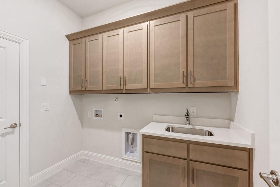 Laundry room with light wood cabinets, utility sink, and washer and dryer hookups on white tile floor