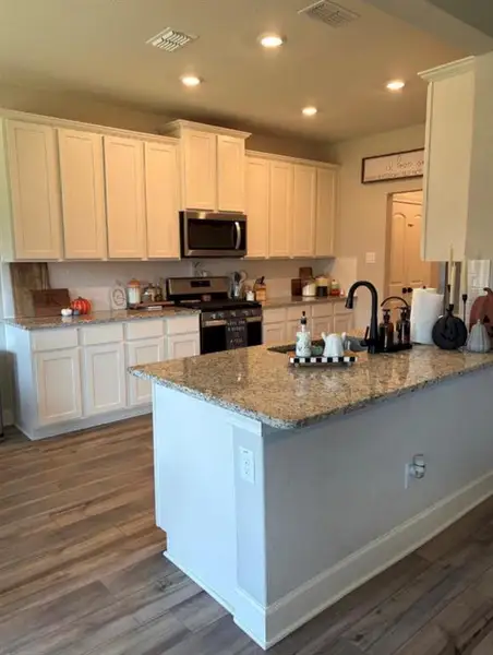 Kitchen featuring extensive white cabinetry, granite countertops, a stainless steel microwave, and wood-finish flooring