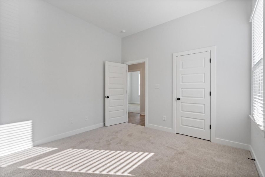 Neutral wall finishes with a vaulted ceiling, plush carpeting, paneled interior doors, and window blinds