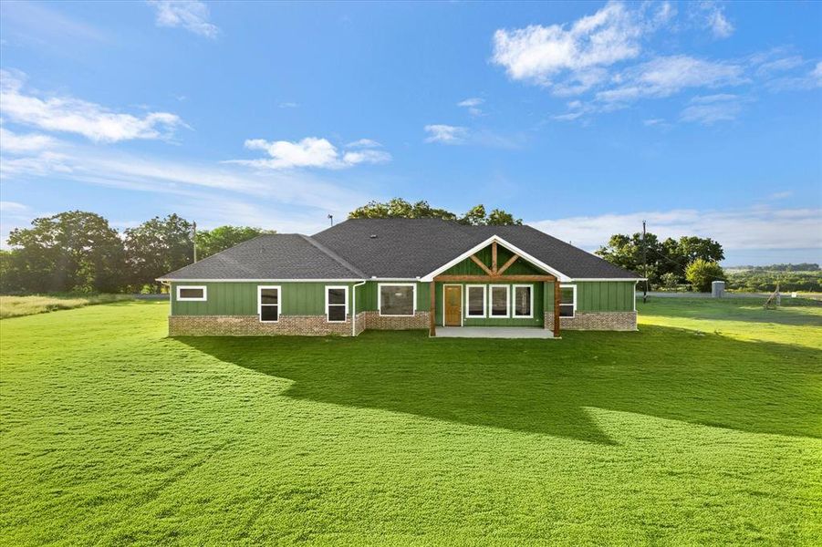 Back of property with a patio area, a yard, board and batten siding, and a shingled roof Back of property with a patio area, a yard, board and batten siding, and a shingled roof