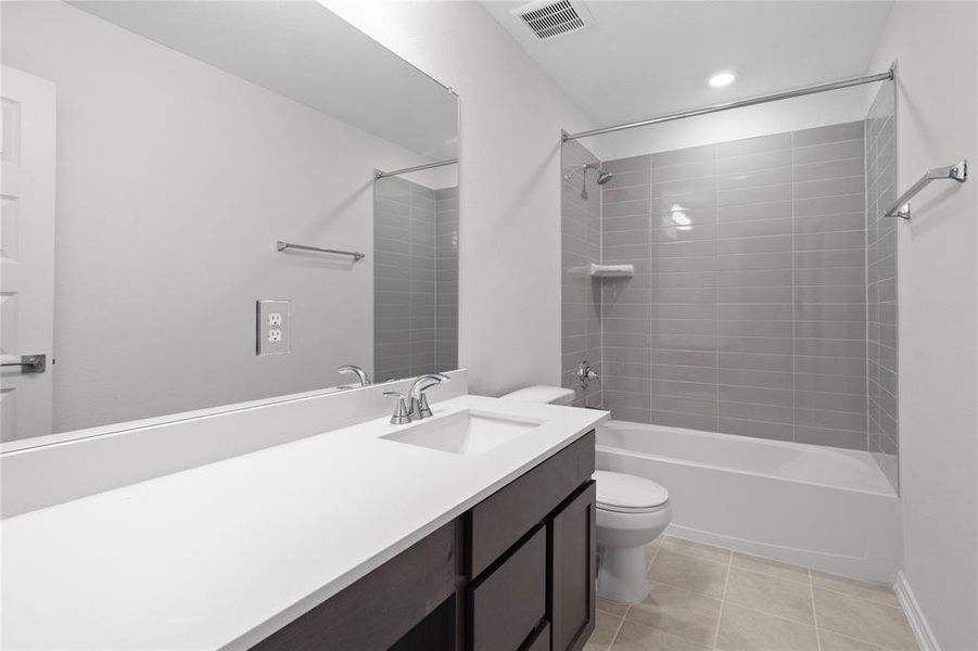 Secondary bath features tile flooring, bath/shower combo with tile surround, stained wood cabinets, beautiful light countertops, mirror, sleek fixtures and modern finishes.