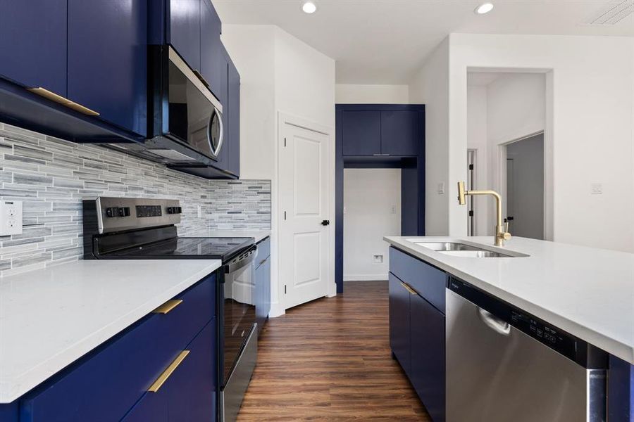 Kitchen featuring blue cabinets, appliances with stainless steel finishes, dark wood-style flooring, light stone counters, and recessed lighting