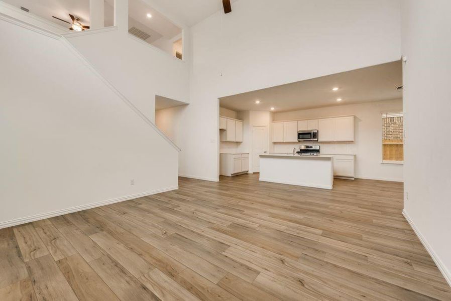 Unfurnished living room featuring a high ceiling, light hardwood / wood-style flooring, and ceiling fan