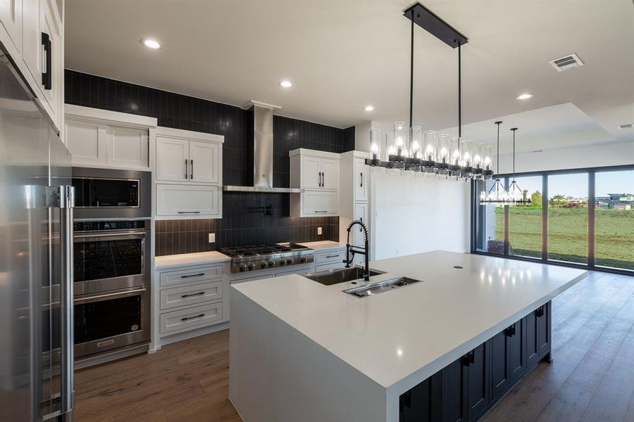 Kitchen with a large island, white cabinets, sink, and wall chimney exhaust hood