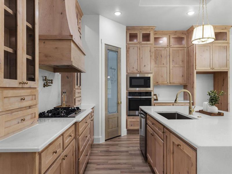 Kitchen featuring glass insert cabinets, wood finished floors, light stone countertops, stainless steel appliances, and recessed lighting