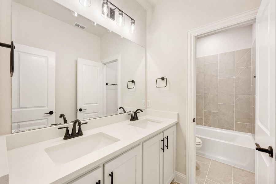 Bathroom with double sink vanity, white cabinets, large mirror, and tiled tub-shower combo with black hardware accents