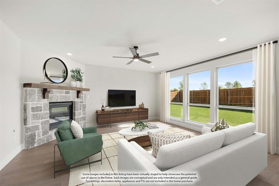 Living room with stone fireplace, ceiling fan, and large windows overlooking a backyard