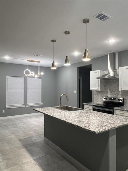 Kitchen featuring white cabinets, light stone counters, wall chimney range hood, stainless steel electric stove, and decorative light fixtures Kitchen featuring white cabinets, light stone counters, wall chimney range hood, stainless steel electric stove, and decorative light fixtures