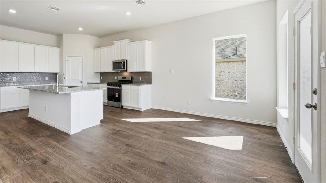 Open concept living area featuring wood-look flooring, a kitchen island with a sink, white cabinetry, and stainless steel appliances Open concept living area featuring wood-look flooring, a kitchen island with a sink, white cabinetry, and stainless steel appliances