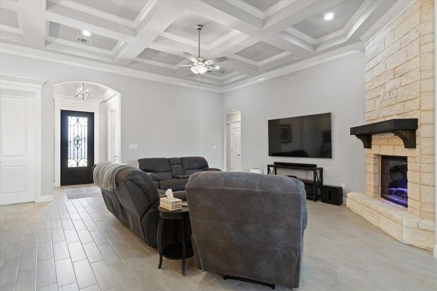 Living area with arched walkways, beam ceiling, a fireplace, visible vents, and light wood-type flooring