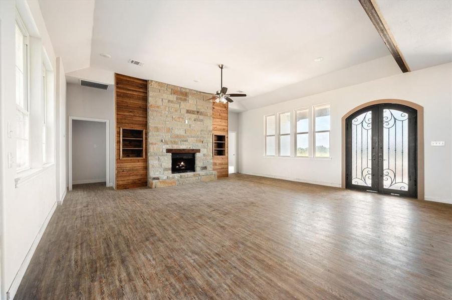 Unfurnished living room featuring ceiling fan, vaulted ceiling with beams, hardwood / wood-style floors, french doors, and a stone fireplace