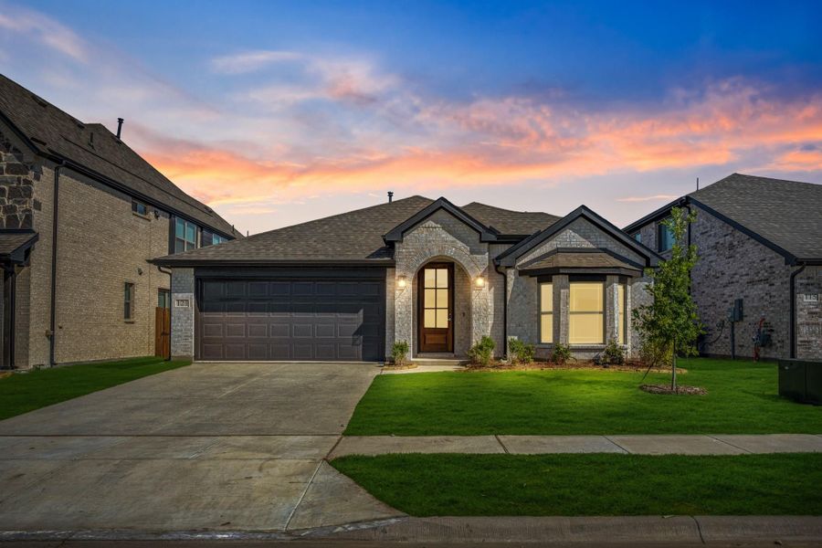 Single-story home with stone exterior, two-car garage, arched entry, and green front lawn at dusk