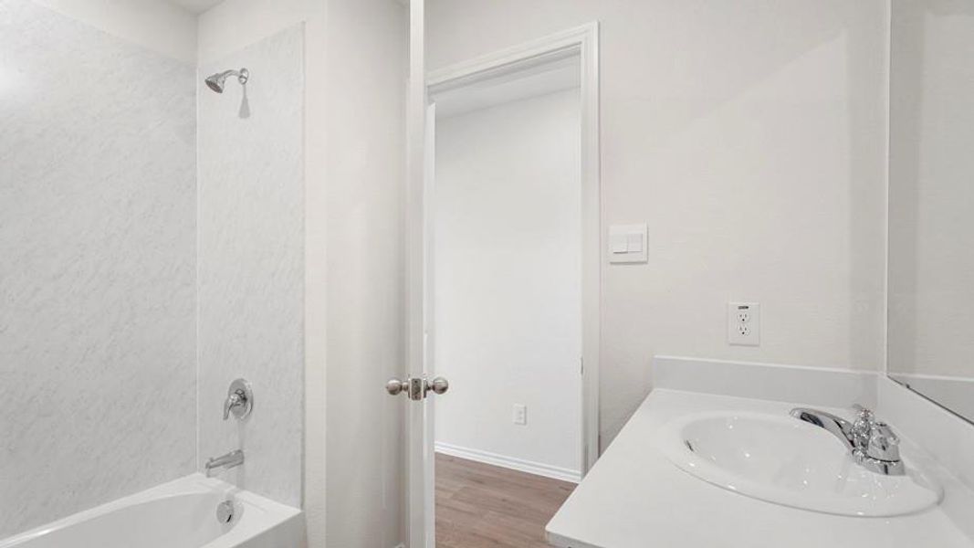 Bathroom featuring a white bathtub with a tile-patterned surround, chrome fixtures, a single vanity with an integrated sink, and a white countertop