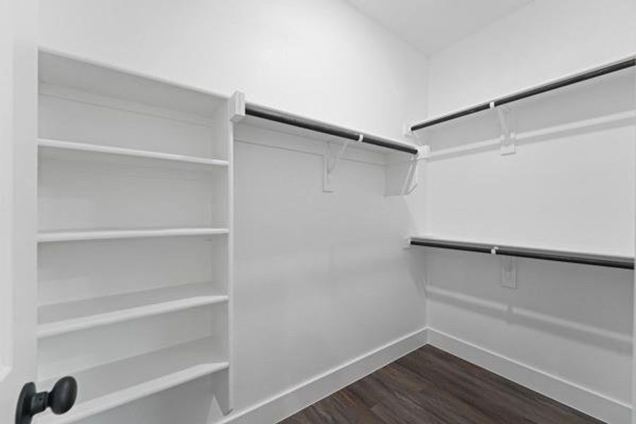 Walk-in closet featuring built-in shelving, multiple hanging rods, white walls, and wood-finish flooring Walk-in closet featuring built-in shelving, multiple hanging rods, white walls, and wood-finish flooring