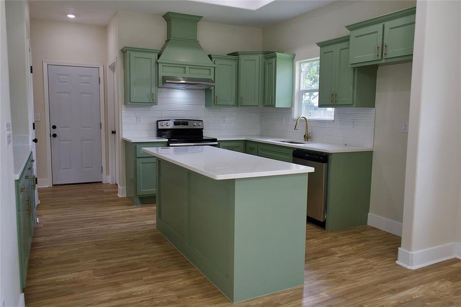 Kitchen featuring green cabinets, a center island, tasteful backsplash, stainless steel appliances, and light wood finished floors