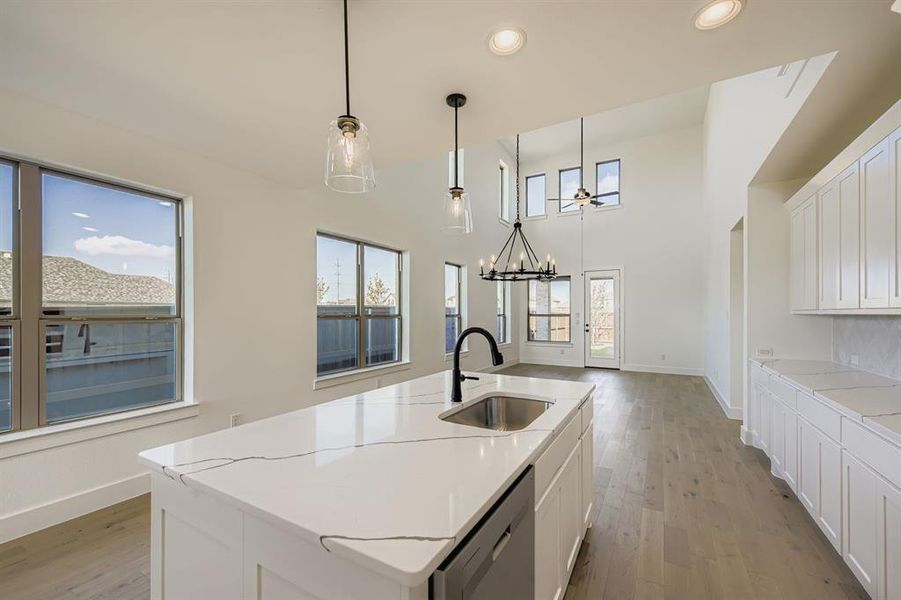 Kitchen with white cabinetry, light wood-style floors, hanging light fixtures, a center island with sink, and dishwasher