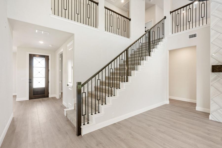 Two-story foyer with carpeted staircase, black iron railings, light wood floors, and glass-panel front door