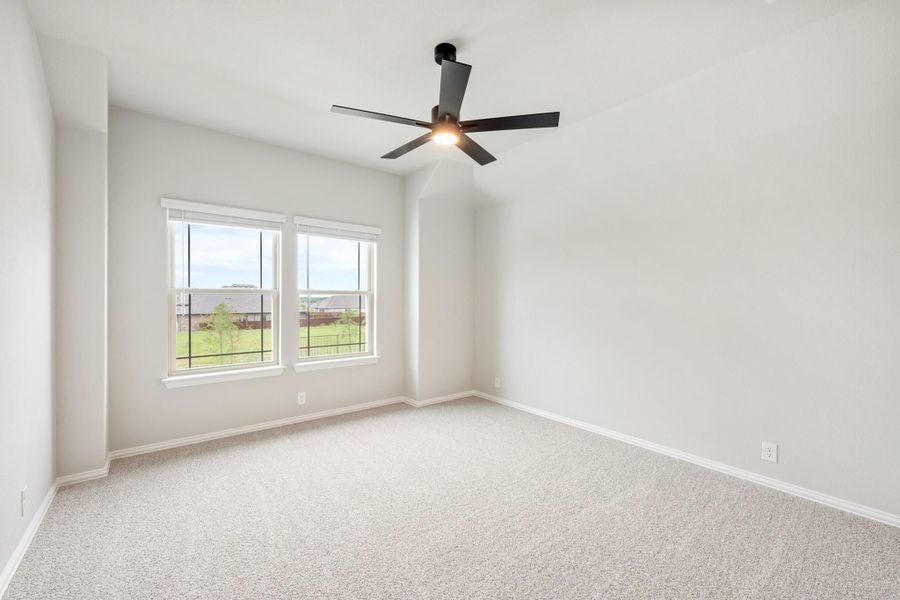 Empty bedroom with carpet flooring, vaulted ceiling, black ceiling fan, and two windows with backyard view