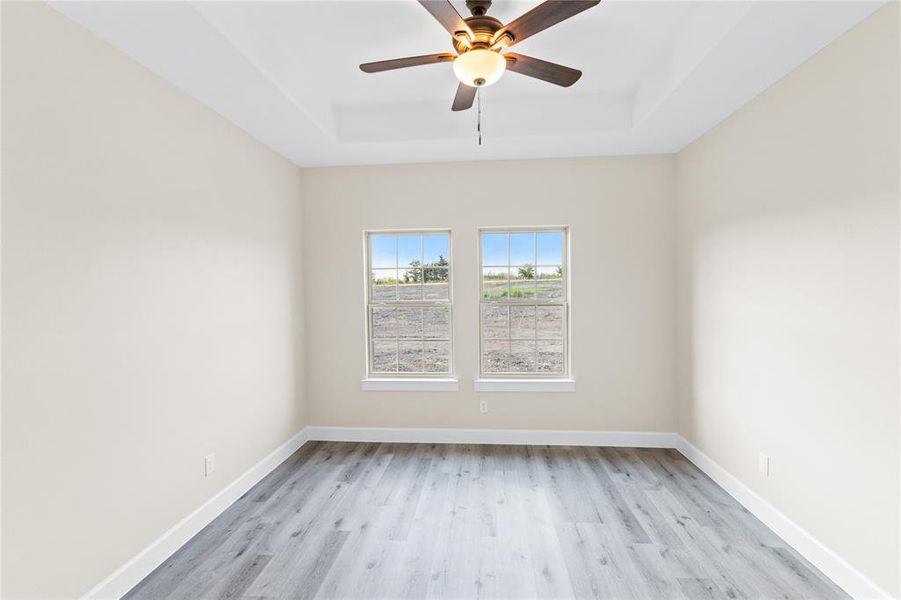 Unfurnished room featuring ceiling fan, a tray ceiling, and light hardwood / wood-style floors