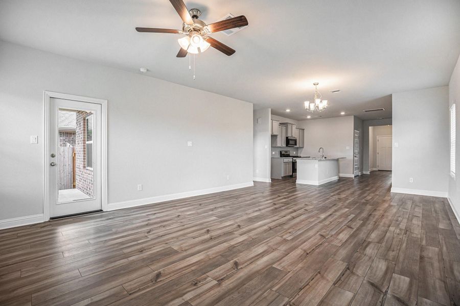 This photo showcases a spacious, open-concept living area with luxury vinyl plank flooring, neutral walls, and a ceiling fan. The modern kitchen features stainless steel appliances, an island, and elegant lighting. A door leads to an outdoor area, enhancing the space's natural light.