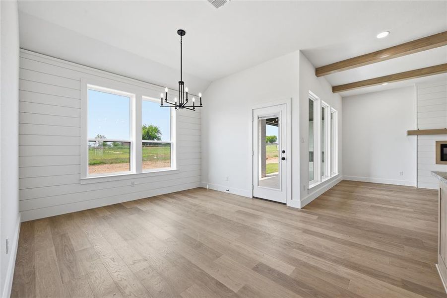 Unfurnished dining area with lofted ceiling with beams, a fireplace, light wood-style floors, healthy amount of natural light, and suspended lighting Unfurnished dining area with lofted ceiling with beams, a fireplace, light wood-style floors, healthy amount of natural light, and suspended lighting