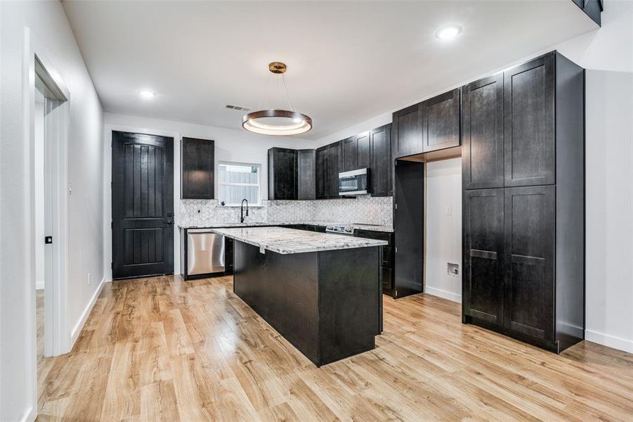 Kitchen featuring stainless steel appliances, light stone counters, a center island, decorative backsplash, and light wood-type flooring