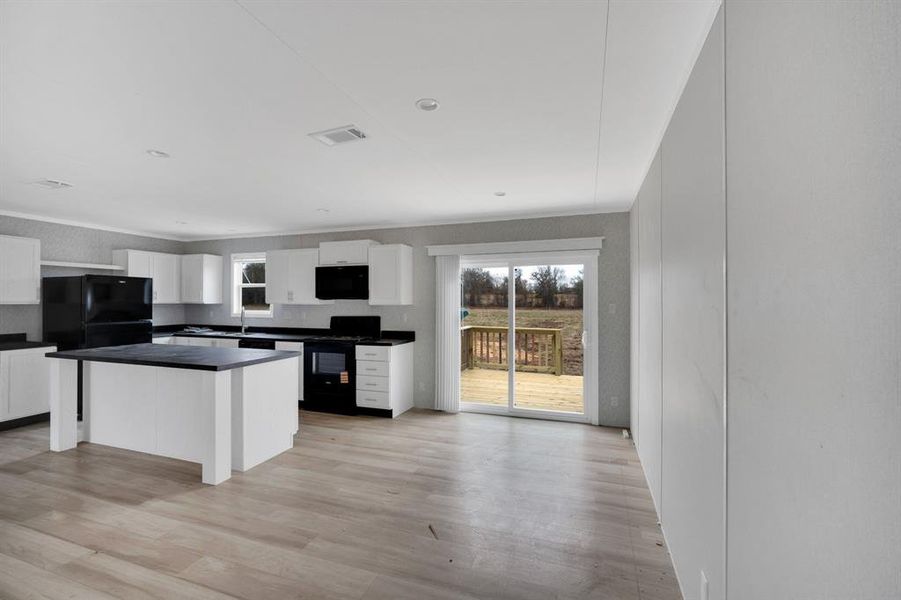 Kitchen with black appliances, white cabinetry, dark countertops, crown molding, and plenty of natural light